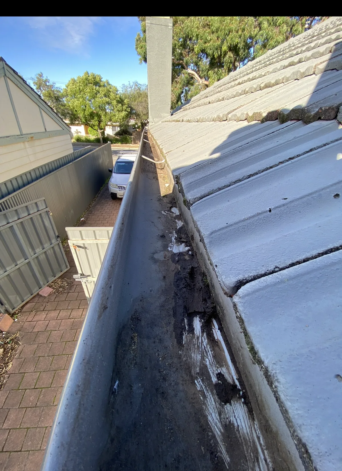 Black sludge and debris built up along a tile-roof gutter before cleaning